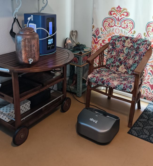 A cosy corner with the HH600 hydrogen unit on a wooden cart, a chair, and the Prife iTeraCare on the floor